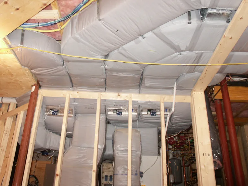Insulated ductwork being installed between basement joists